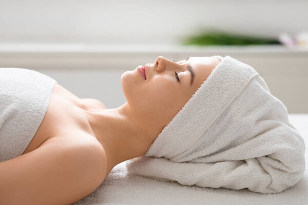 Beautiful young woman resting at spa, laying on massage table