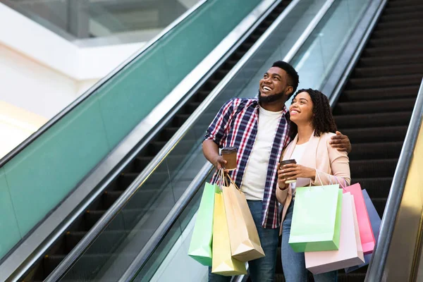 Feliz casal negro descendo a escada rolante depois de compras bem sucedidas no shopping — Fotografia de Stock