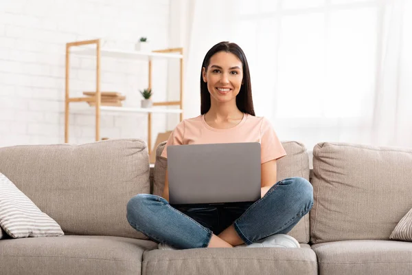 Mujer usando el teléfono portátil sentado en el sofá, mirando a la cámara — Foto de Stock