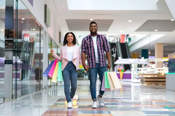 Concept commercial. Heureux couple noir marchant dans le centre commercial portant des sacs à provisions colorés — Photo