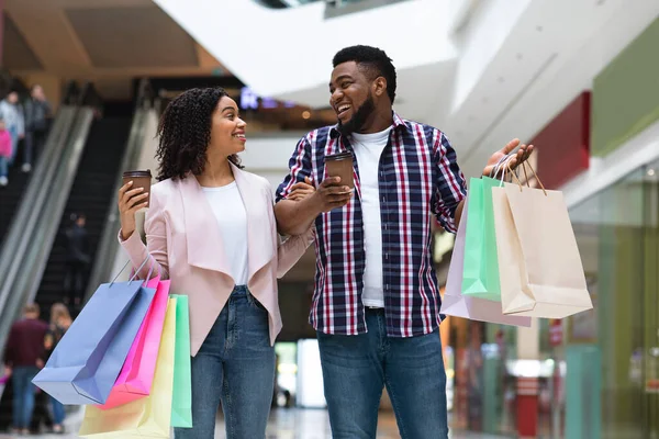 Black millennial couple walking in mall with shopping bags and coffee — Stock Photo, Image