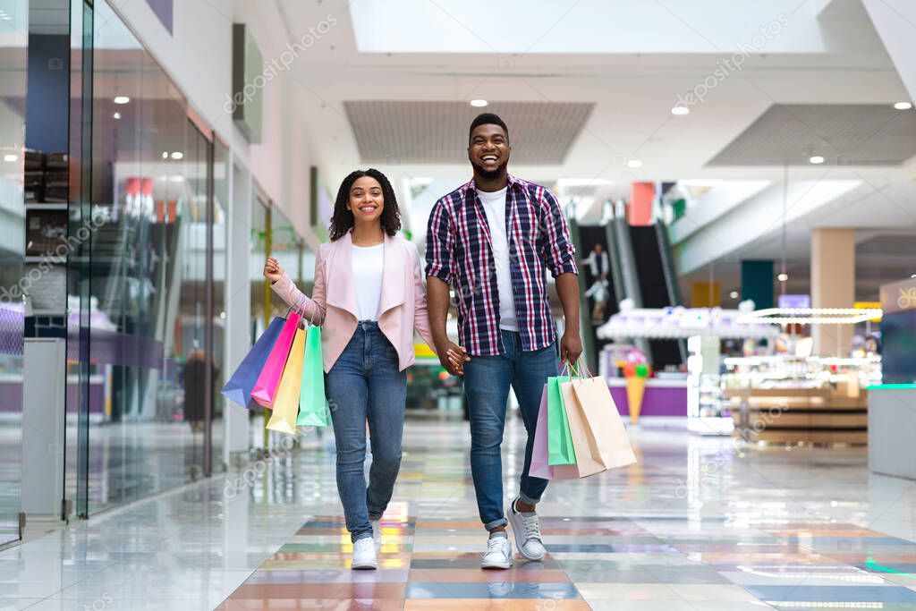Shopping Concept. Happy Black Couple Walking In Mall Carrying Colorful Shopper Bags