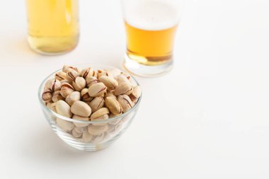 Bira gelenekleri ve aperatifler. Cam tabakta kabuklu şam fıstıkları. Yakınlarda bitmemiş bira ve şişe var.