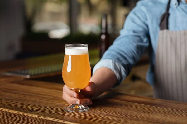 Kunst van het brouwen. Barman in schort op houten tafelglas licht pils met schuim — Stockfoto