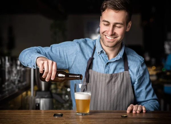 Bartender pours glass of beer. Smiling handsome guy with bottle at bar