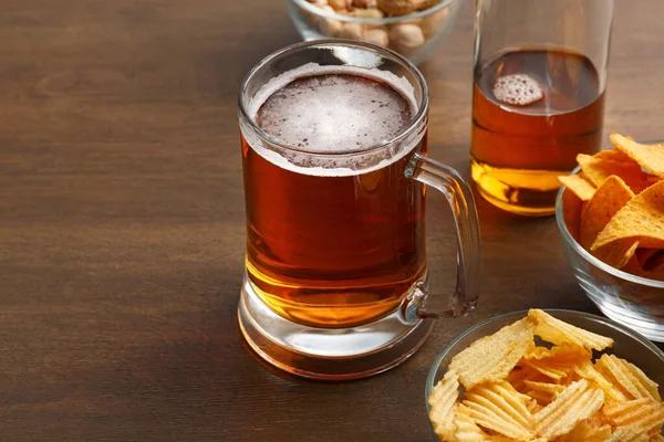 Bardak ve şişe köpüklü parlak, taze bira. Şam fıstığı, cips ve cam tabakta cips. — Stok fotoğraf