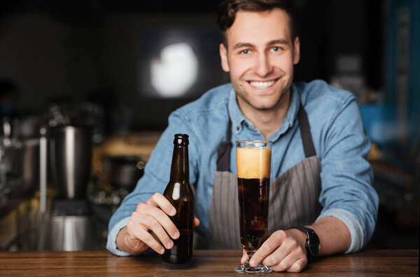 Fresh beer for client. Smiling bartender pours dark drink in high glass
