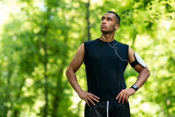 Millennial black athlete listening to music after his morning run at city park, free space — Stock Photo, Image