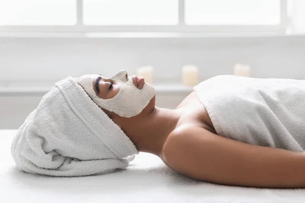 Black girl with white face mask resting on massage table — Stock Photo, Image