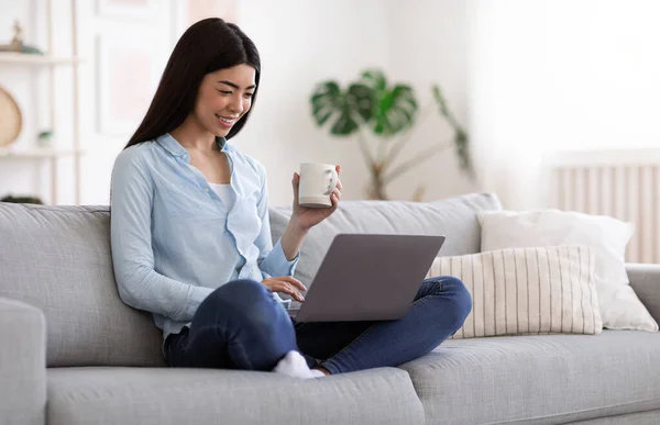 Домашний отдых. Молодая азиатка отдыхает с ноутбуком и кофе дома — стоковое фото