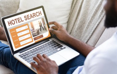 Siyah adam evde takılıyor, tatil planlıyor, dizüstü bilgisayar kullanıyor.