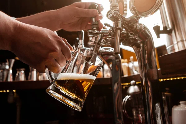 Pracující barman. Barman nalévá pivo z kohoutku ve skleněném hrnku v interiéru hospody — Stock fotografie