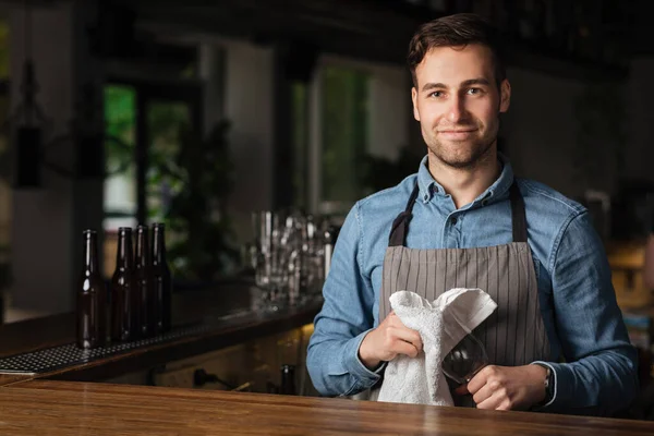 Servicio en el pub. Barman limpia el vidrio vacío, de pie en el bar en el interior — Foto de Stock