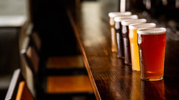 Festa com amigos no pub. Fila de copos de cerveja de diferentes tipos no balcão de bar no interior — Fotografia de Stock