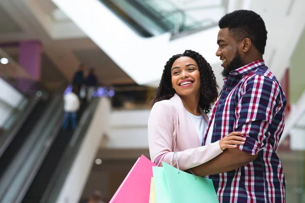 Ευτυχισμένο μαύρο ζευγάρι απολαμβάνει ψώνια μαζί στο σύγχρονο εμπορικό κέντρο, χαμογελώντας και αγκαλιάζοντας — Φωτογραφία Αρχείου