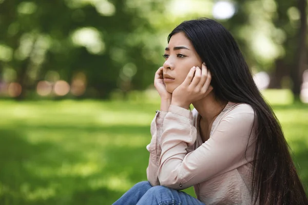 孤独。沮丧的女孩坐在公园的草坪上，想着什么 — 图库照片