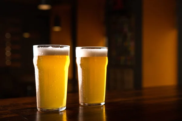 Peça cerveja no pub. Copos de cerveja na mesa no interior do pub escuro — Fotografia de Stock