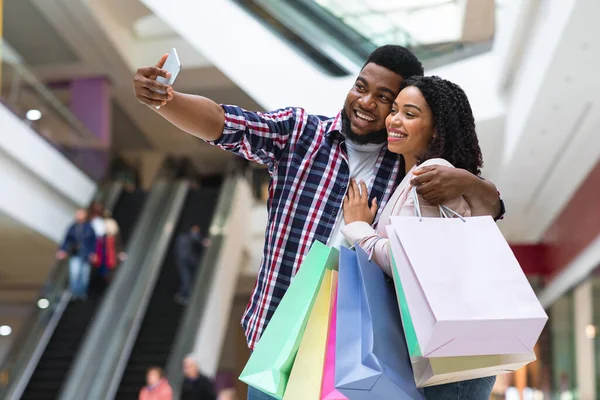 Winkelplezier. Joyful zwart paar nemen selfie in winkelcentrum, holding shopper tassen — Stockfoto