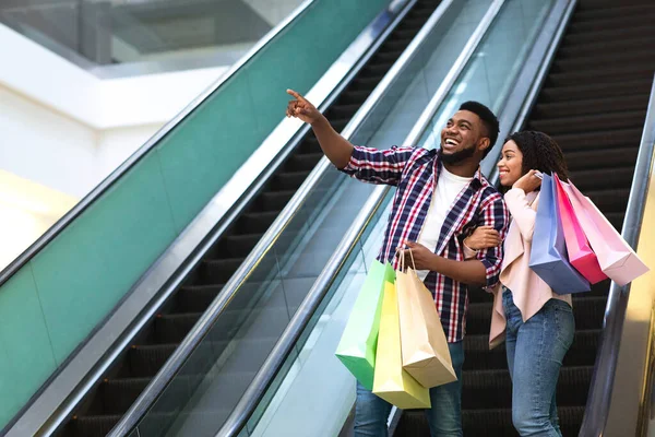 Conceito de vendas. feliz casal preto com sacos de compras indo para baixo na escada rolante — Fotografia de Stock