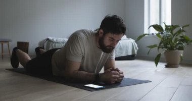 Genç adam kalas egzersizi yapıyor ve mobil uygulama kullanıyor.