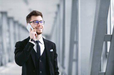 Akıllı telefondan konuşan gülen iş adamı gözlük takıyor.