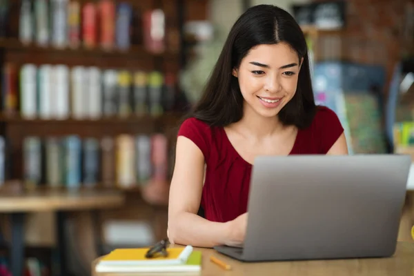 Educación en línea. Sonriendo chica asiática estudiando con el ordenador portátil mientras está sentado en la cafetería —  Fotos de Stock