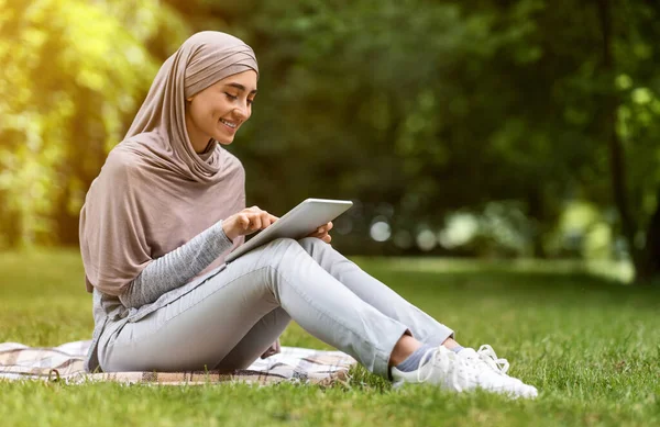 Mujer musulmana joven usando tableta digital en el parque —  Fotos de Stock