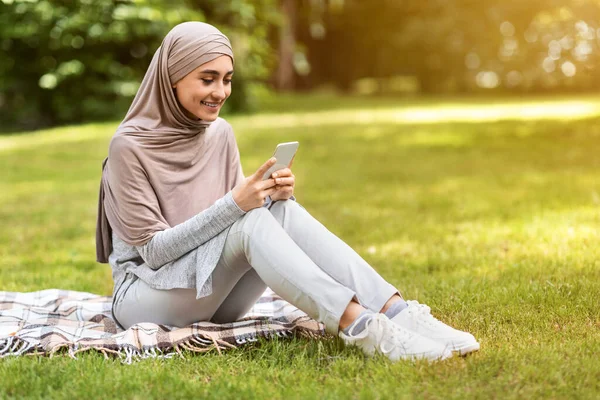 Chica árabe usando el teléfono inteligente mientras pasa tiempo en el parque —  Fotos de Stock