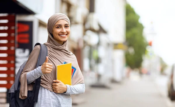 Chica árabe bonita con bloc de notas y mochila mostrando el pulgar hacia arriba — Foto de Stock