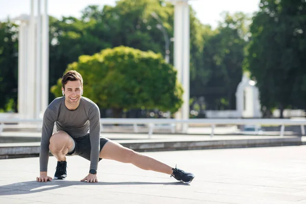 Прогрівайтеся перед бігом у парку. Чоловік у спортивній формі робить вправи для ніг — стокове фото