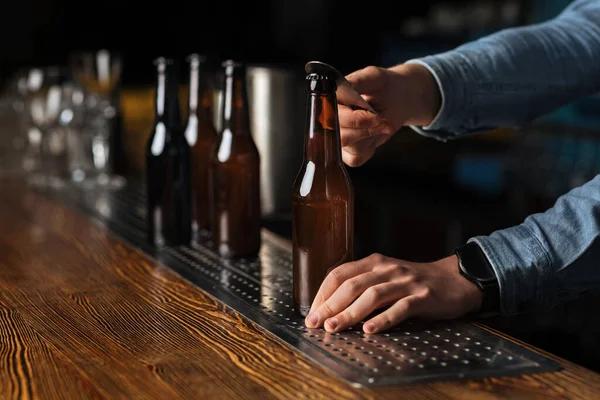 Industria cervecera. Cantinero abre botella de cerveza sin etiqueta en barra de madera contador — Foto de Stock