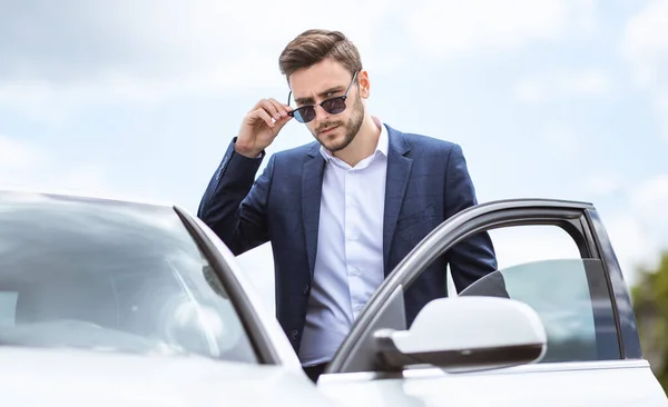 Ernsthafter CEO in offizieller Kleidung und Sonnenbrille steigt in der Innenstadt der modernen Stadt in sein Auto — Stockfoto