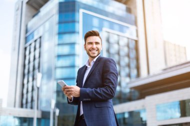 Modern metropolün şehir merkezinde akıllı telefonlu mutlu bir CEO.