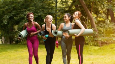 Şehir parkında sabah yogasından önce iletişim kuran ve gülen neşeli çok kültürlü kadınlar.