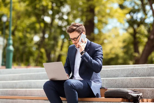 Empreendedor ocupado falando no telefone celular e trabalhando com computador portátil nas escadas do parque — Fotografia de Stock