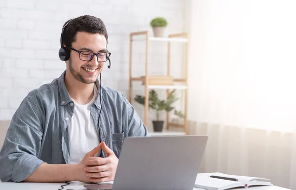 Aprende inglés en línea. Sonriente tipo con auriculares mirando a la computadora portátil, hablando con el profesor — Foto de Stock