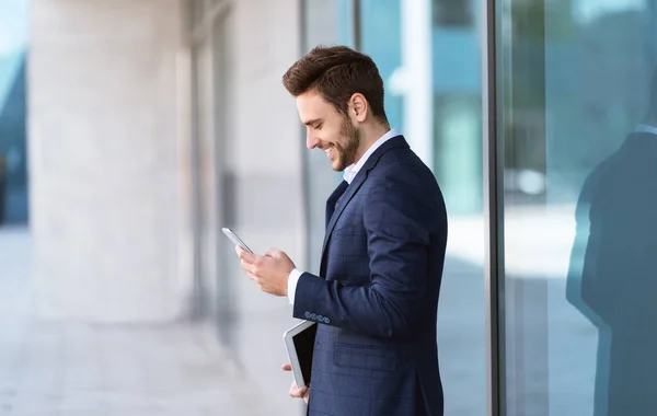 CEO sorrindo comunicando com o parceiro no telefone celular perto arranha-céu na cidade grande, espaço livre — Fotografia de Stock