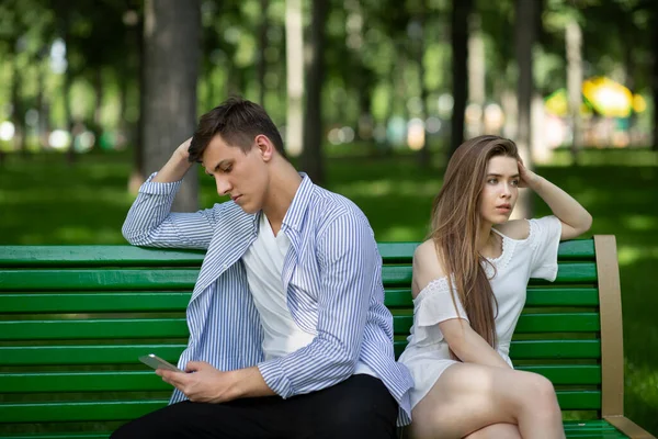Una cita aburrida. Aburrido joven molesto con su novio jugando juegos en el teléfono inteligente en el parque — Foto de Stock