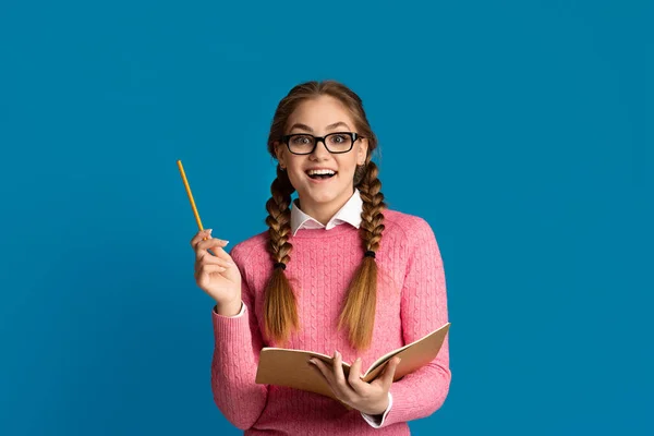 Vilken bra idé. Överraskad tonåring flicka i glasögon håller penna och anteckningsbok i händerna — Stockfoto