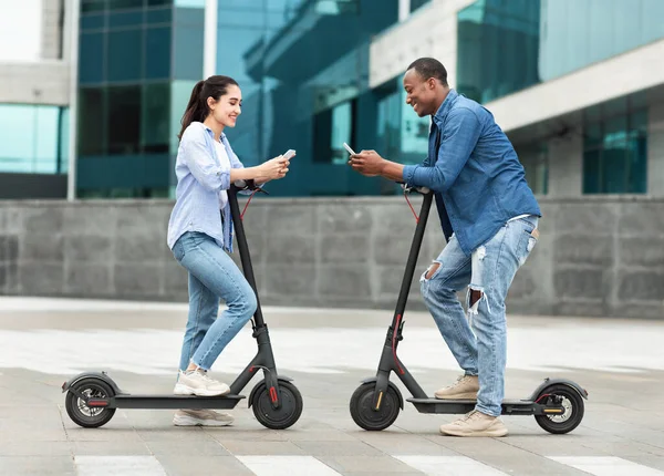 Friends having ride on motorized kick scooters, holding phones — Stock Photo, Image