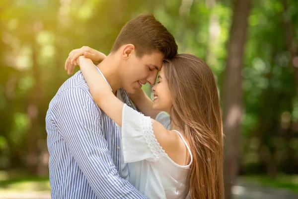 Pareja joven abrazándose y tocándose la frente en una cita romántica en el parque — Foto de Stock