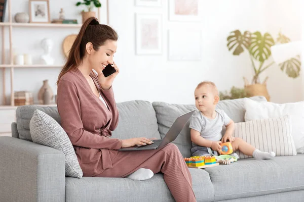 Ocupada mamá trabajando con el ordenador portátil y el teléfono celular mientras cuida del bebé — Foto de Stock