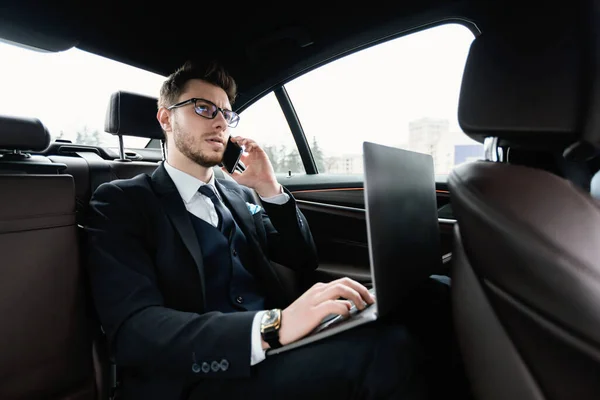 Ung affärsman talar i telefon i bilen med sin dator — Stockfoto