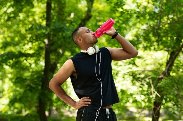 Durstiger junger Sportler trinkt nach seinem Training im Park Wasser aus der Flasche — Stockfoto