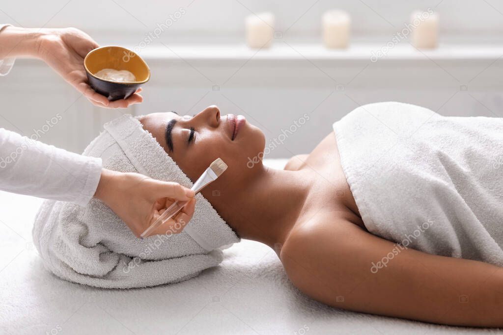 Beautician holding bowl with face mask next to black lady