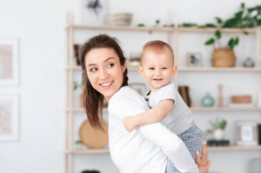 Doğum günün kutlu olsun. Anne, sevimli bebeğiyle evde oynuyor, onu sırtında taşıyor.