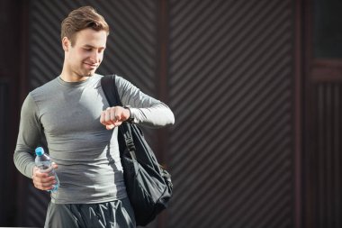 Genç gülümseyen adam spor çantasıyla eğitime gider ve spor giyim kuşamında elinde iz sürücüye bakar.