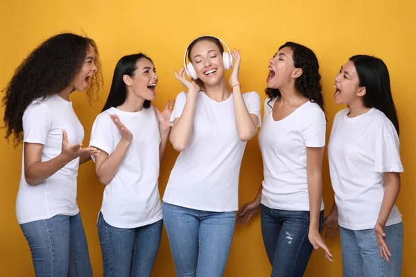 Fille dans les écouteurs ne pas entendre ses amis crier, fond jaune — Photo