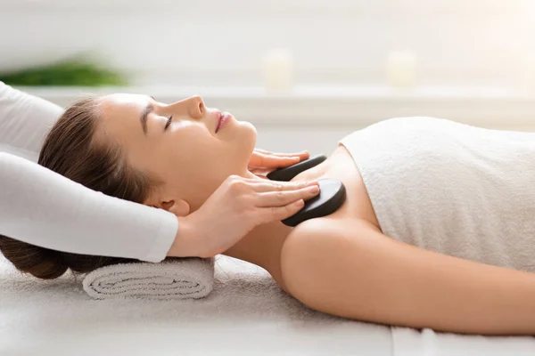 Terapeuta de massagem colocando pedras quentes nos ombros da mulher — Fotografia de Stock