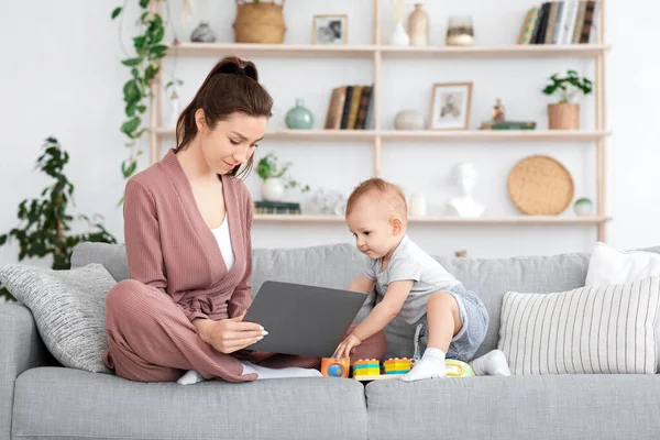 Freelancing During Maternity Leave. Young Mom Working On Laptop With Baby Around